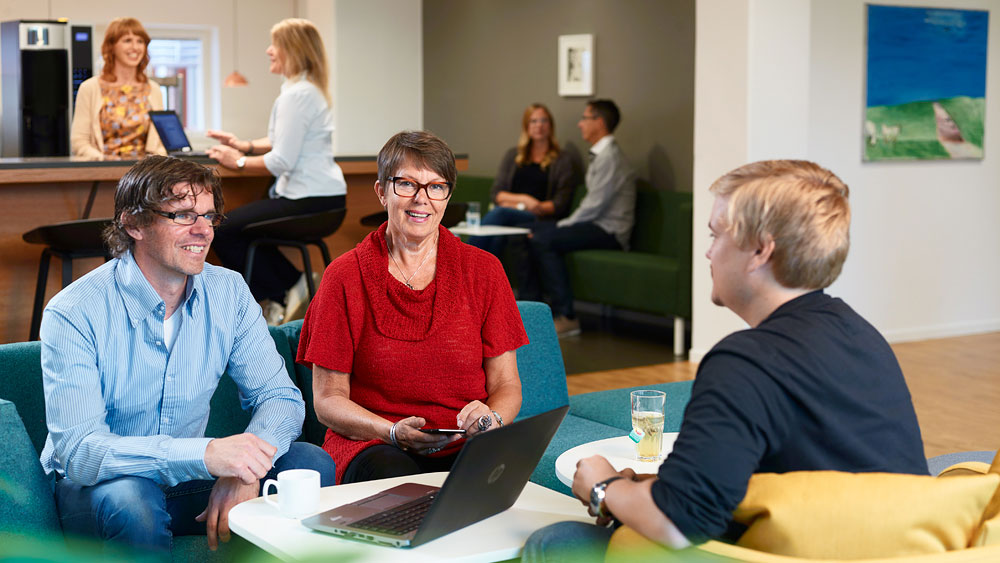 Tre medarbetare sitter vid ett bord på jobbet och pratar