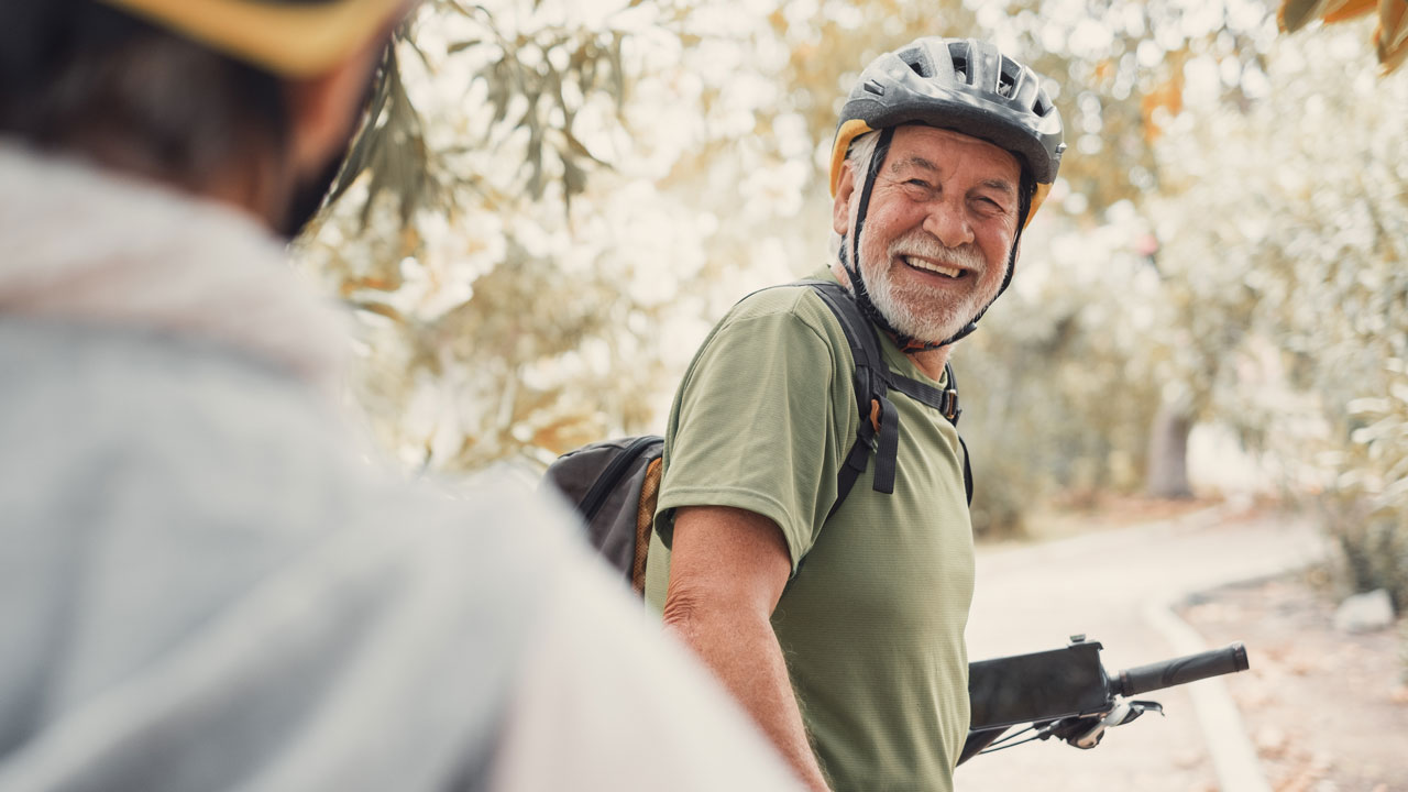 Äldre man står vid en cykel och ler mot en annan person